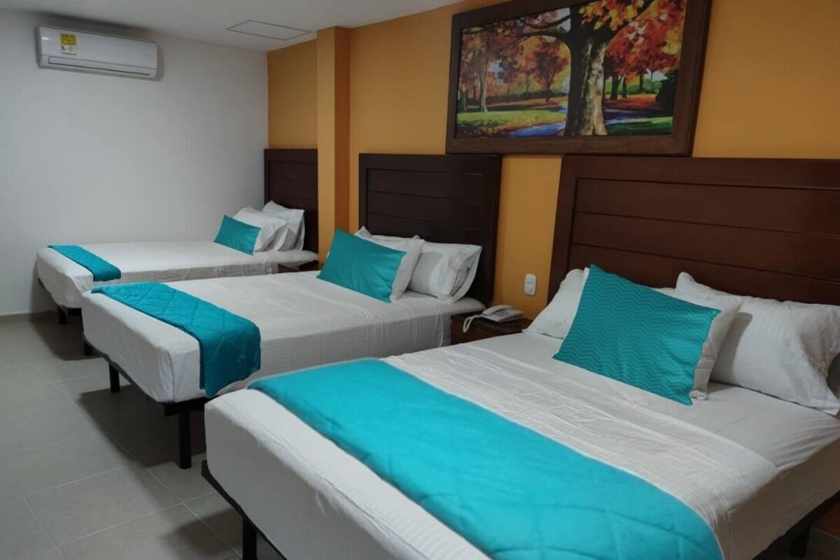 A hotel room with three beds, each with white bedding and teal accents.