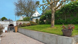 A gravel driveway leading to a house with a concrete retaining wall, a brick oven, and a large potted plant.