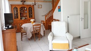 A living room with a dining table, wooden cabinets, a white armchair, and a staircase.