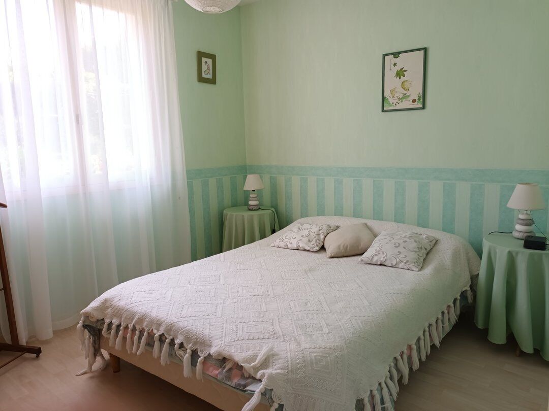A bedroom with a bed, two bedside tables, a window with curtains, and a wall with a picture.