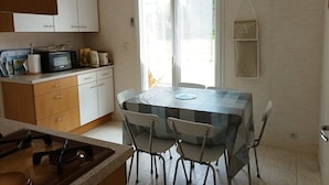 A kitchen with a dining table, chairs, cabinets, a microwave, and a hanging shelf.