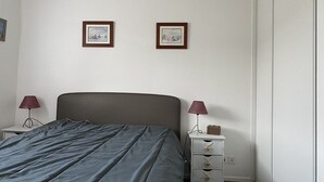 Ein Schlafzimmer mit einem Bett, zwei Nachttischen, einem Beistelltisch und zwei gerahmten Bildern an der Wand.