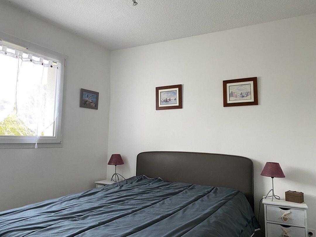 Une chambre à coucher avec un lit, deux tables de chevet avec des lampes et trois tableaux encadrés accrochés au mur.