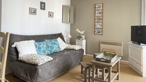 Ein modernes Hotelzimmer mit einer grauen Couch, einem kleinen Tisch, einem Fernseher und einem an der Wand befestigten Bilderrahmen.