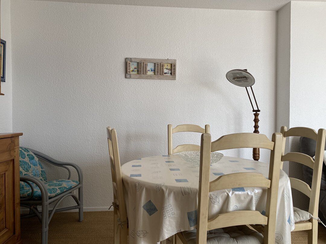 A dining area with a round table covered by a tablecloth, surrounded by wooden chairs.