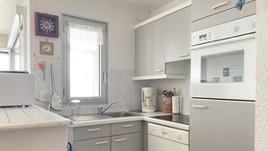 Eine Küche mit weißen Schränken, einem Geschirrspüler, einer Kaffeemaschine und einem Fenster mit Vorhang.