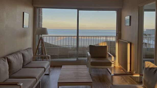 Een moderne woonkamer met een bank, een salontafel en een stoel, gericht op een balkon met uitzicht op de oceaan.