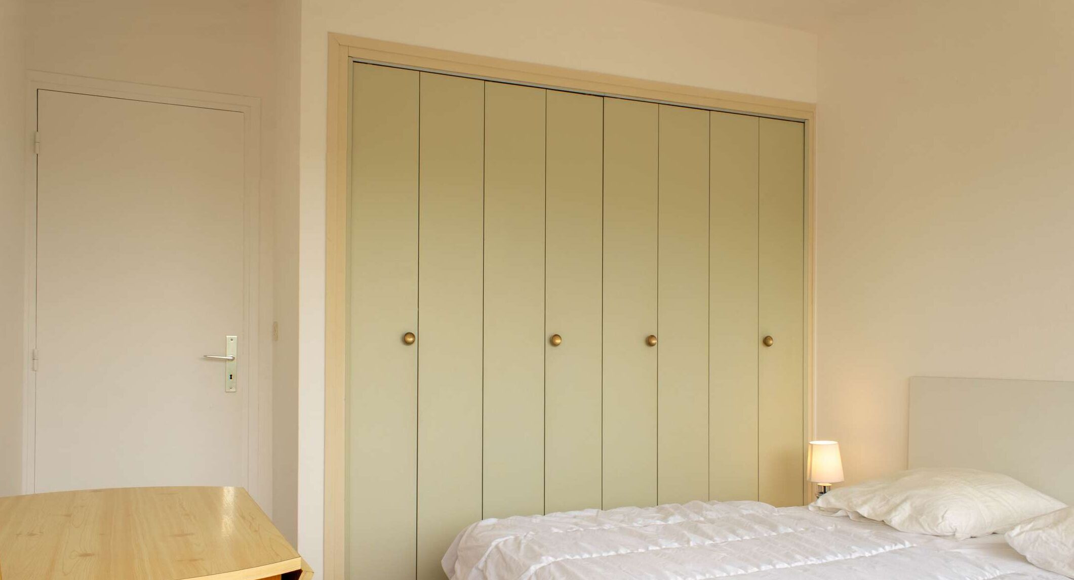 Un dormitorio con cama, mesita de noche y armario de cinco puertas.