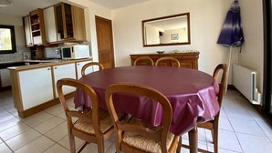 A dining area with a round table covered in a purple tablecloth, surrounded by wooden chairs with woven seats. A wooden cabinet with glass doors is to the left, and a mirror hangs on the wall above a wooden cabinet. - House with terrace in Erquy | 6 guests | Ref 603 (ERQUY)