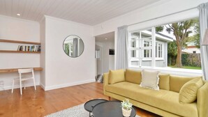 Una sala de estar moderna con un sofá amarillo, un espejo redondo y una pequeña mesa con una planta.