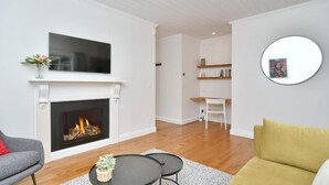 Una sala de estar con chimenea, un televisor de pantalla plana encima, un sofá, una mesa de centro y un espejo redondo en la pared.