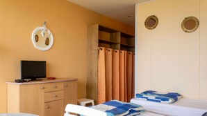 Un dormitorio con cama, televisor sobre una cómoda, armario y ventana con cortina.