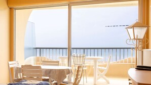 Un balcón con mesa y sillas, una lámpara y vista al mar.