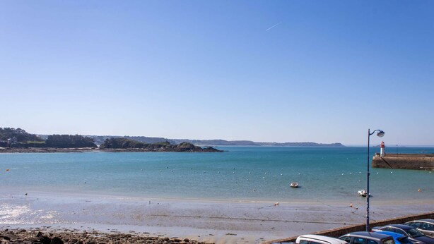 A coastal view with a clear sky, calm sea, and a lighthouse in the distance.