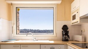 A kitchen with a large window, a sink, a coffee maker, a toaster, and a view of a coastal town.