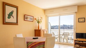 A room with a dining table, chairs, a TV, and a view of the city through large windows.
