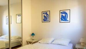 A hotel room with a bed, a nightstand with a lamp, and two framed abstract art pieces on the wall.