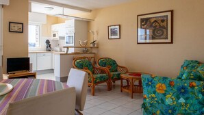 A compact living space with a kitchenette, a dining area with a table and chairs, and a seating area with a sofa and two wicker chairs.