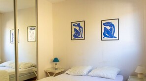 A hotel room with a bed, a nightstand with a lamp, and two framed abstract art pieces on the wall. - Sea-view apartment in Erquy | 2 guests | Ref 50 (ERQUY)