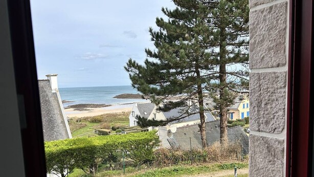 A coastal view from a window overlooking a beach, a stone building, and a large pine tree. - Sea-view house in Erquy | 8 guests | Ref 70 (ERQUY)
