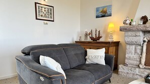A grey sofa with orange trim, a patterned floor, a framed picture, a ship model, and a stone fireplace. - Sea-view house in Erquy | 8 guests | Ref 70 (ERQUY)