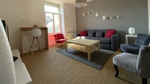 A living room with a grey sofa, a red chair, a wooden coffee table, and a grey armchair. There is a wall-mounted sign that reads "Lands & Bruyes". - Apartment near beach in Erquy | 5 guests | Ref 653 (ERQUY)