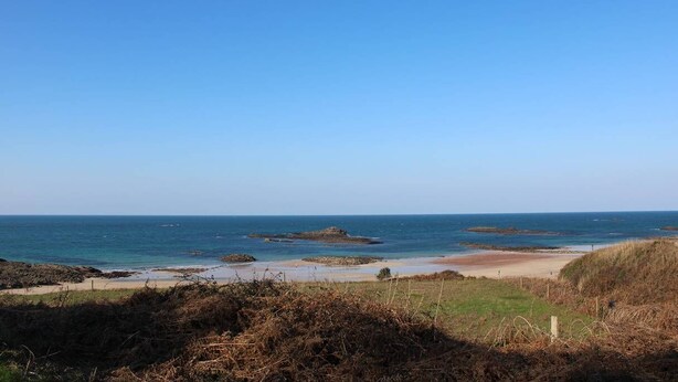 Een kustlandschap met heldere lucht, rotsformaties en een zandstrand.