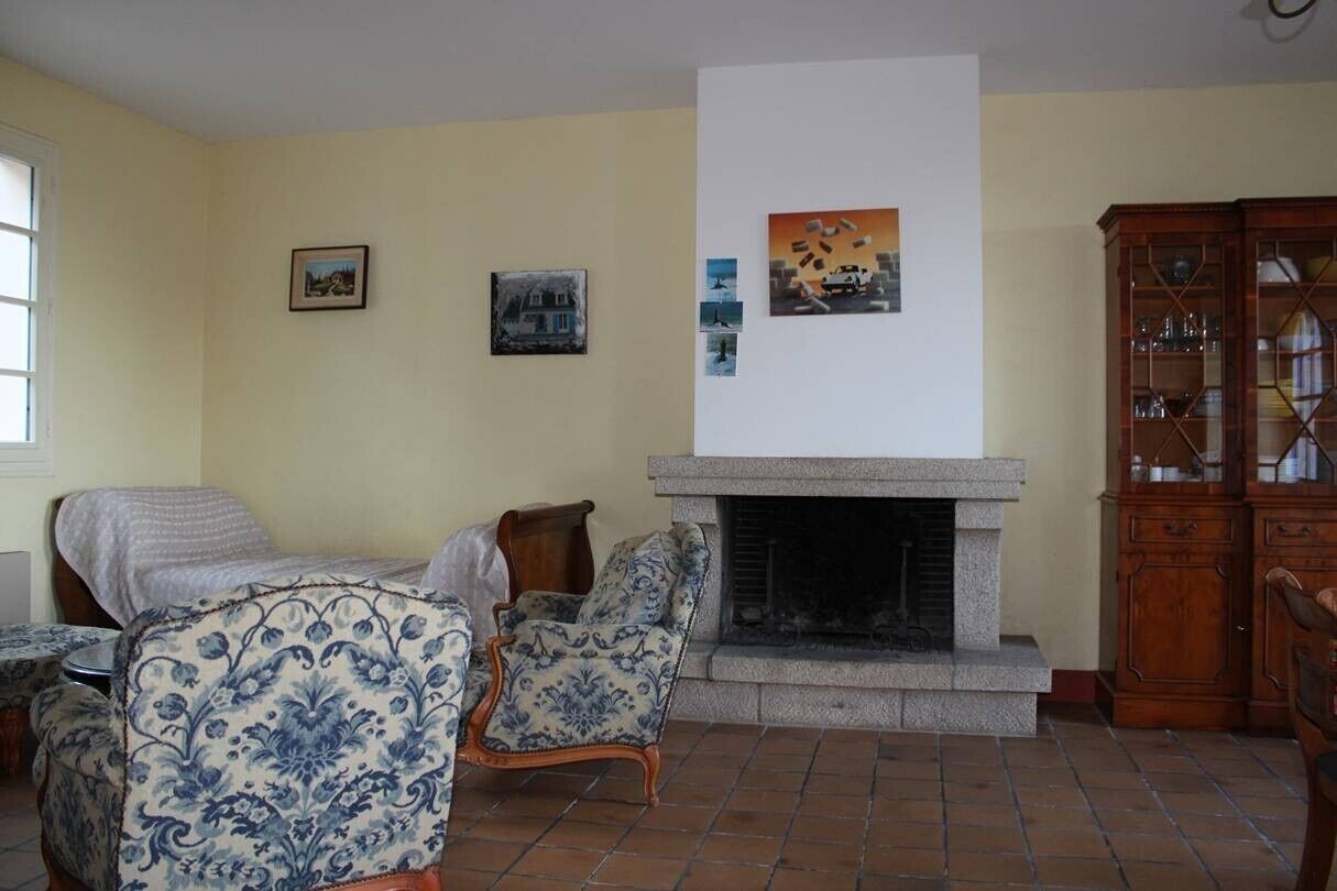 Un salon doté d’une cheminée, de deux fauteuils à motifs, d’un meuble en bois et d’œuvres d’art accrochées au mur.