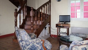 Een woonkamer met een houten trap, een bank, een glazen salontafel en een televisie.