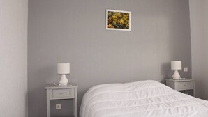 Une chambre à coucher avec un lit, deux tables de chevet avec des lampes, un petit tableau au mur et un mur gris.