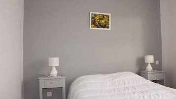 A bedroom with a bed, two bedside tables with lamps, a small picture on the wall, and a gray wall.