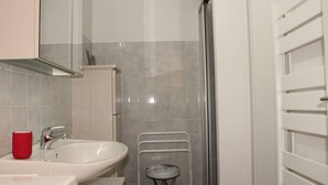 Une salle de bain avec un lavabo blanc, un verre rouge et un espace douche.