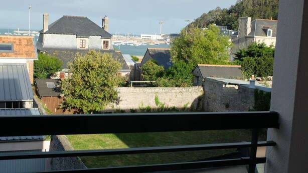 Vue depuis un balcon donnant sur une marina, avec des bateaux, un mur de pierre et des immeubles d’habitation.
