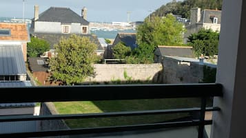 A view from a balcony overlooking a marina with boats, a stone wall, and residential buildings.