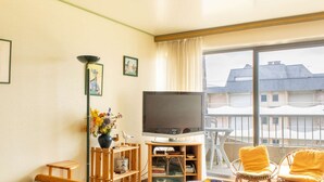 En stue med TV, bogreol, vase med blomster og balkon med stole.