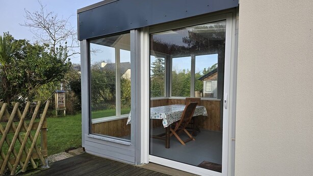 A covered patio area with a table and chairs, a wooden deck, and a view of the surrounding garden and trees. - House with garden in Erquy | 6 guests | Ref 602 (ERQUY)