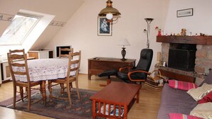 A cozy living room with a dining table, chairs, a sofa, a fireplace, and a lamp.