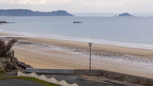 A beach with a concrete walkway, a lamp post, and distant islands. - Sea-view apartment in Erquy 50 m from the beach | 4 guests | Ref 411 (ERQUY)
