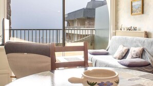 Een woonkamer met uitzicht op een gebouw en een balkon. Er staat een tafel met een schaal en een stoel.