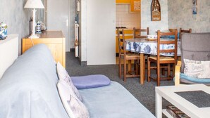 Een gezellige woonkamer met een bank, een eettafel met stoelen en een keuken die zichtbaar is door een open deur.