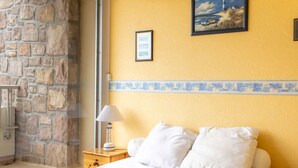 Een slaapkamer met een stenen muur, een bed met wit beddengoed, een nachtkastje met een lamp en een lijst met een afbeelding aan de muur.