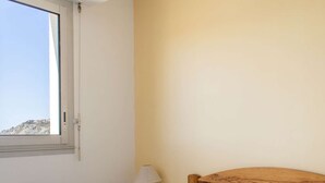 A bedroom with a bed, a nightstand, a lamp, and a window with a view of a hill. - Sea-view apartment in Erquy | 4 guests | Ref 514 (Erquy)