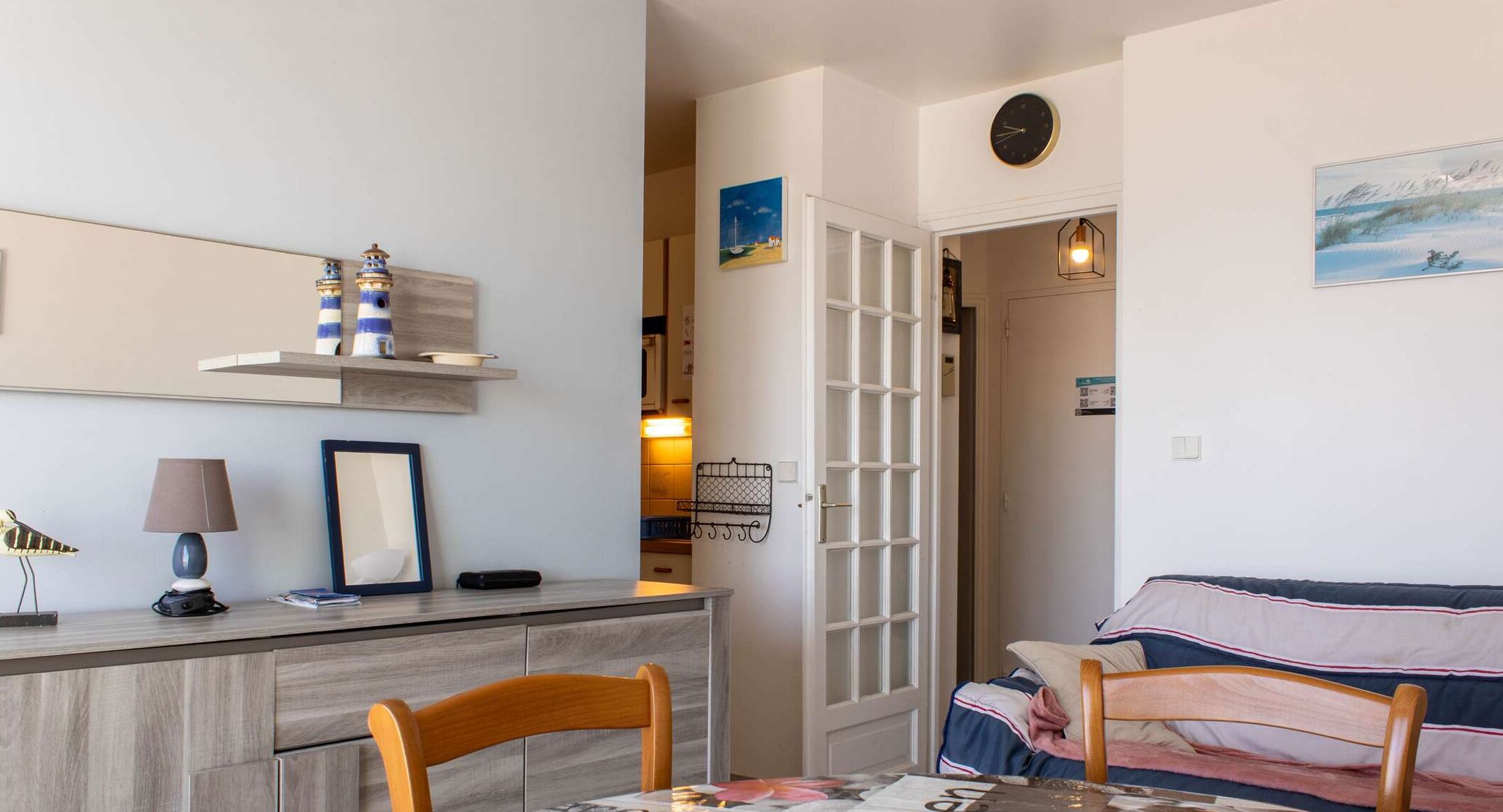 Een gezellige kamer met een houten bureau, een stoel, een bed met gestreept beddengoed en een deur naar een andere kamer.