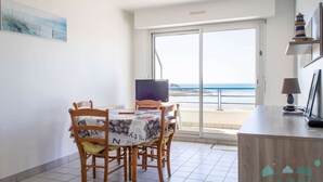 A dining area with a table and chairs, a television, and a view of the beach through a sliding glass door. - Sea-view apartment in Erquy | 4 guests | Ref 514 (Erquy)