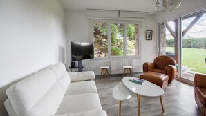Moderni olohuone, jossa on valkoinen sohva, ruskea nahkainen nojatuoli, valkoinen sohvapöytä ja litteänäyttöinen televisio.