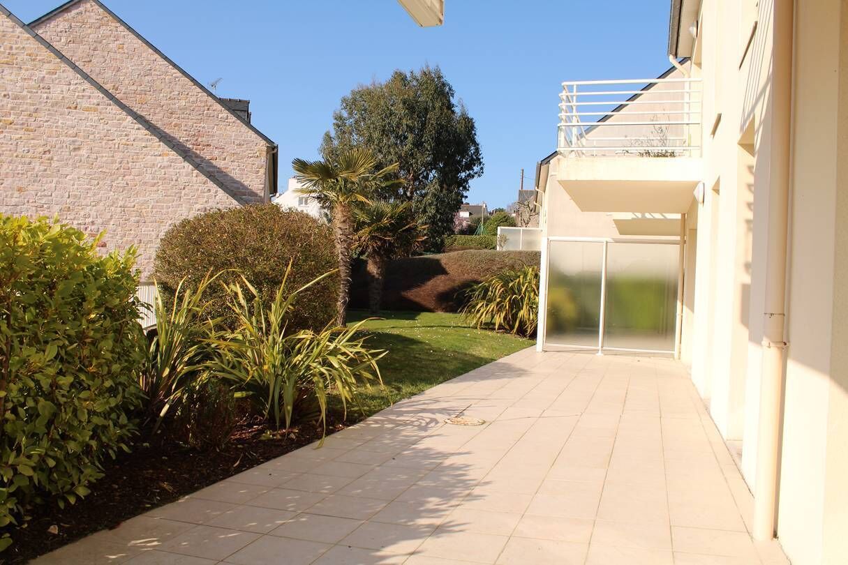 Ein Weg führt zu einem Gebäude mit Balkon, umgeben von viel Grün und blauem Himmel.