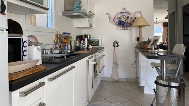 Une cuisine moderne avec des armoires blanches, un plan de travail noir et un sol carrelé. On y trouve une cuisinière, un évier et une fenêtre au-dessus du plan de travail.