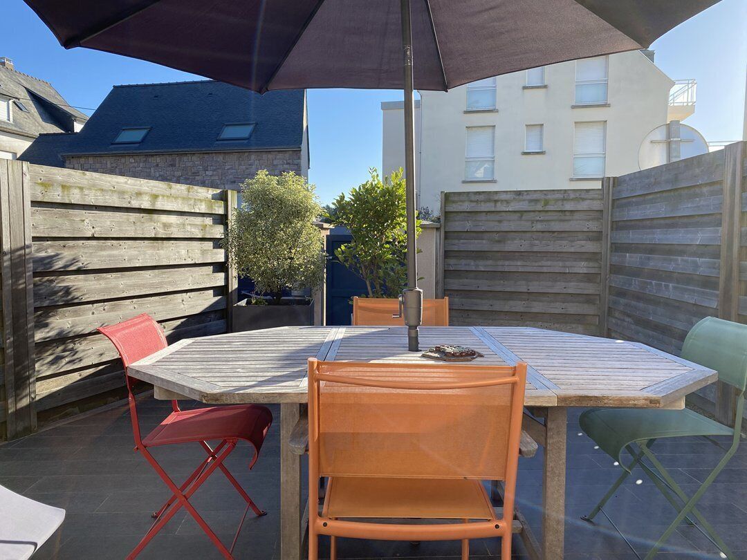 Une terrasse extérieure avec une table et des chaises en bois, un grand parasol et une vue sur les bâtiments voisins.