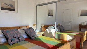 Une chambre avec deux lits, chacun agrémenté de draps colorés et d’oreillers à motifs, un grand miroir et une porte visible au fond.
