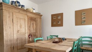 Un coin repas avec une table en bois et des chaises vertes, un meuble en bois orné d’objets décoratifs et des tableaux encadrés accrochés au mur.